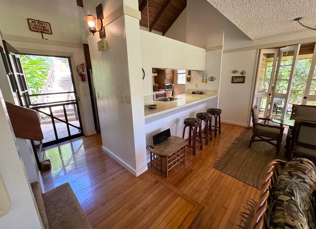 interior space with a textured ceiling, high vaulted ceiling, beam ceiling, and hardwood / wood-style flooring