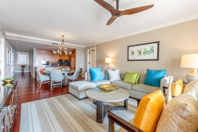 living room featuring crown molding, ceiling fan with notable chandelier, visible vents, and dark wood-style flooring