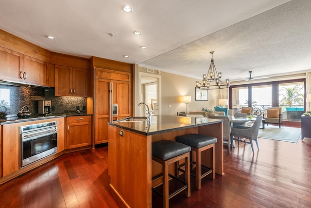 kitchen with oven, a sink, dark wood-style floors, open floor plan, and brown cabinetry