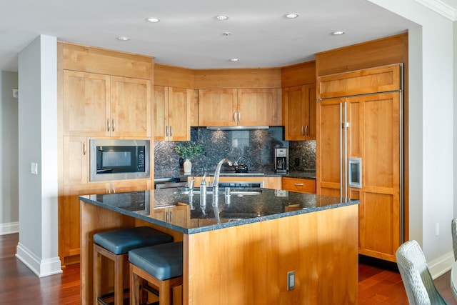 kitchen featuring dark wood-style flooring, tasteful backsplash, built in appliances, and dark stone counters