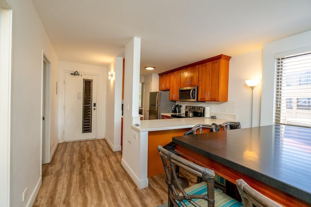 kitchen featuring backsplash, light hardwood / wood-style floors, kitchen peninsula, and stainless steel appliances