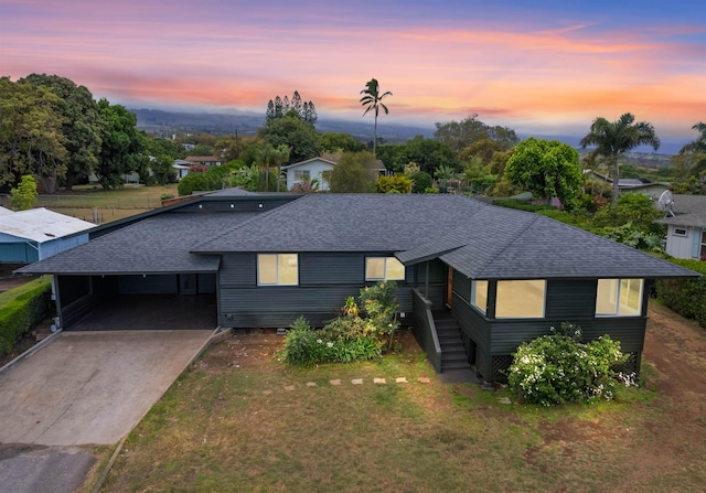 ranch-style house featuring a carport, roof with shingles, driveway, and a front lawn