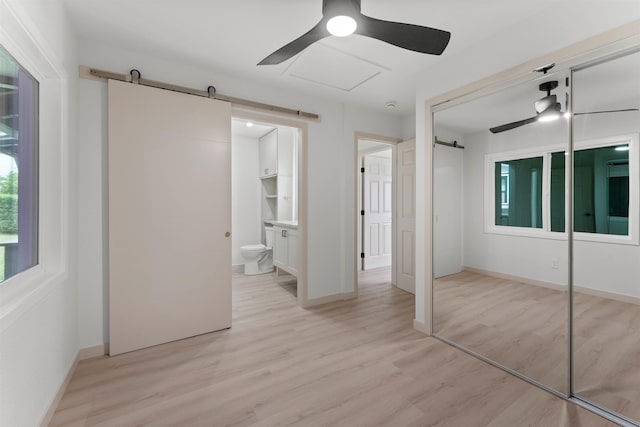 unfurnished bedroom with light wood-type flooring, a closet, a ceiling fan, and a barn door