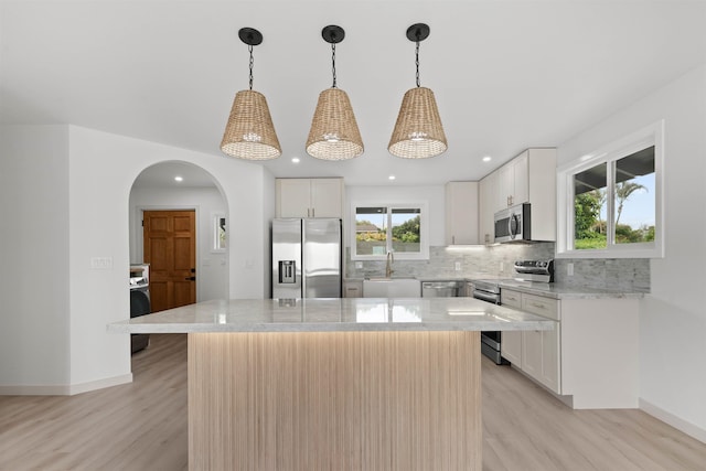 kitchen with tasteful backsplash, light wood-style flooring, appliances with stainless steel finishes, and arched walkways