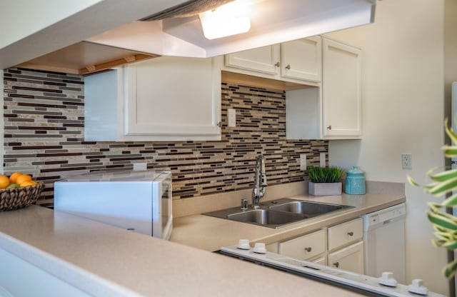 kitchen featuring sink, tasteful backsplash, dishwasher, and white cabinetry