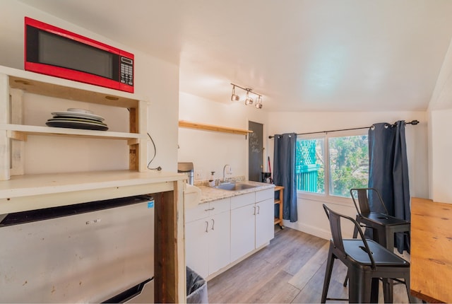 kitchen with light wood-type flooring, lofted ceiling, white cabinets, and sink