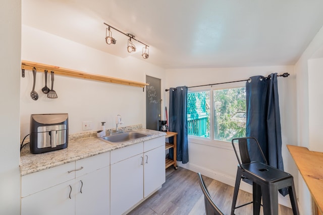 kitchen with lofted ceiling, sink, light hardwood / wood-style flooring, light stone countertops, and white cabinets