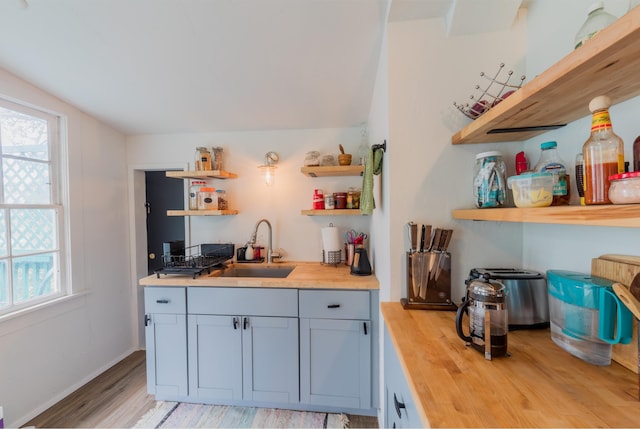 kitchen with vaulted ceiling, light hardwood / wood-style flooring, wooden counters, and sink