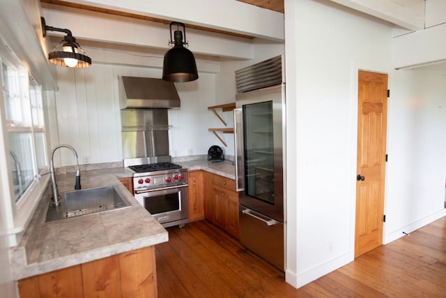 kitchen with hardwood / wood-style floors, premium range, a sink, light countertops, and wall chimney range hood