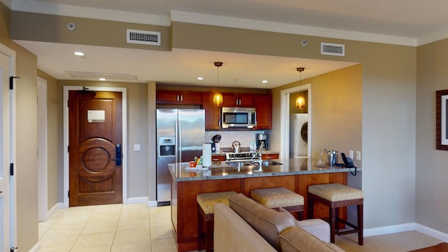 kitchen with hanging light fixtures, washer / dryer, a breakfast bar, light tile patterned floors, and stainless steel appliances