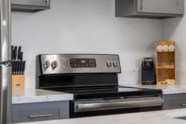 kitchen featuring light stone countertops, electric range, gray cabinets, and backsplash