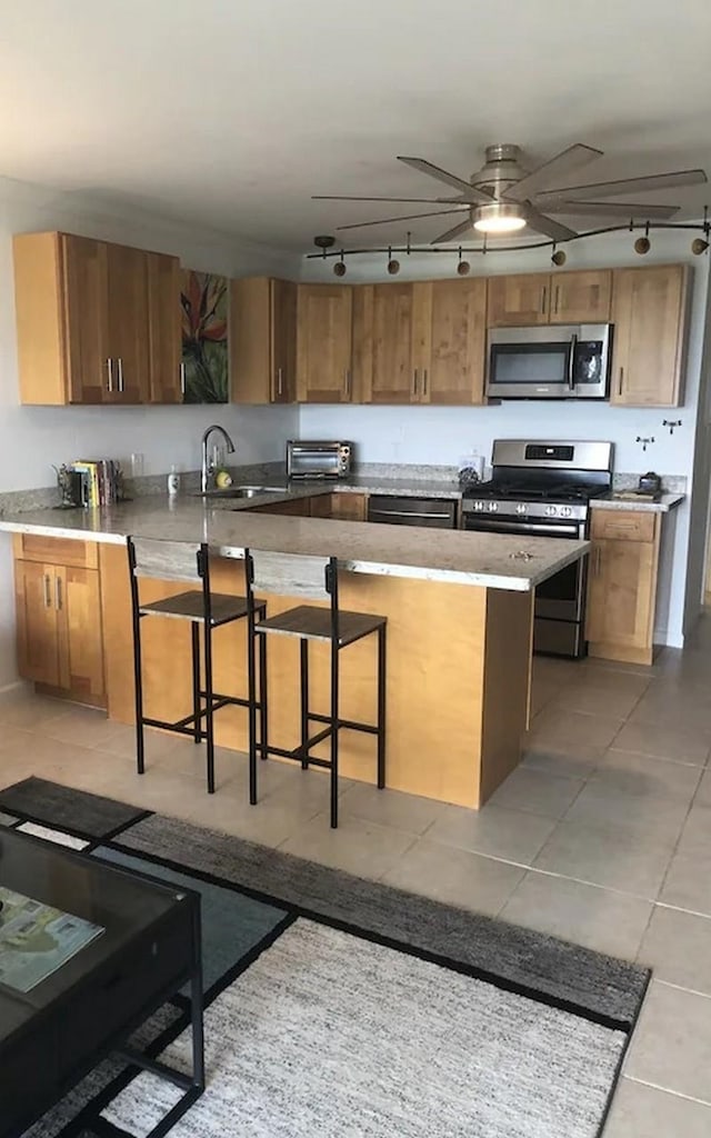 kitchen featuring sink, a breakfast bar area, ceiling fan, stainless steel appliances, and light tile patterned flooring