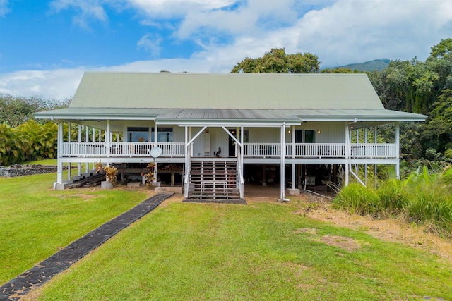 rear view of property with a porch, stairs, metal roof, and a lawn