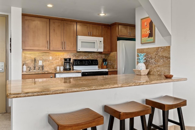 kitchen with white appliances, decorative backsplash, a breakfast bar area, a peninsula, and a sink