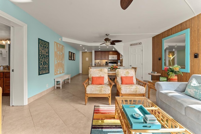 living room with light tile patterned floors, wood walls, a ceiling fan, and baseboards