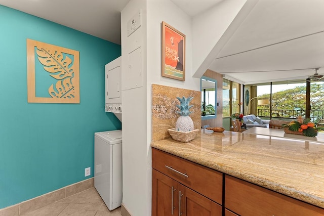 clothes washing area featuring light tile patterned floors, baseboards, and stacked washer and clothes dryer