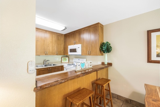 kitchen with a kitchen bar, a sink, white appliances, brown cabinetry, and baseboards