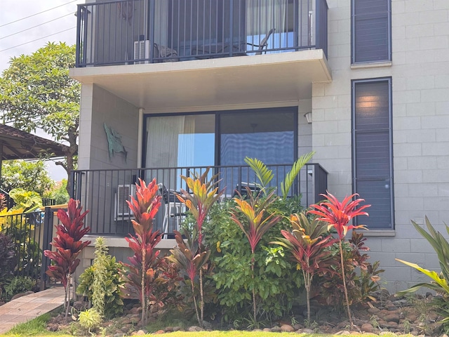view of exterior entry featuring a balcony, concrete block siding, covered porch, and fence