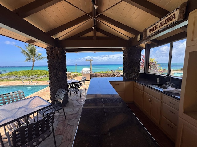 view of patio / terrace featuring a water view, exterior kitchen, an outdoor pool, outdoor dining area, and a sink