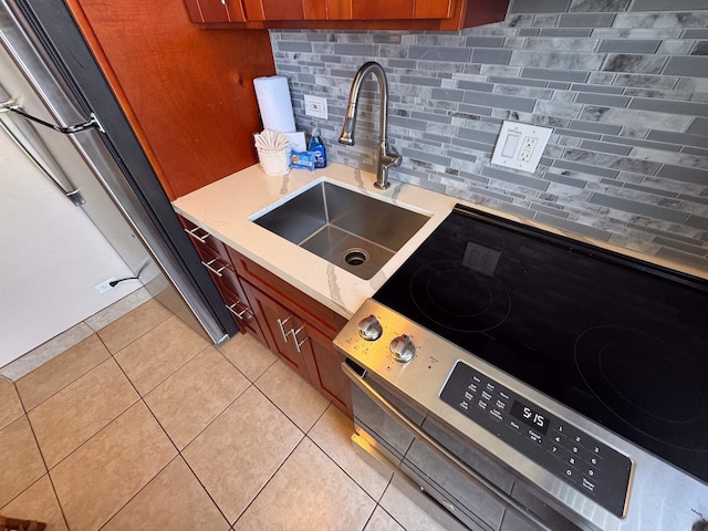 kitchen with decorative backsplash, stainless steel electric stove, a sink, light tile patterned floors, and freestanding refrigerator