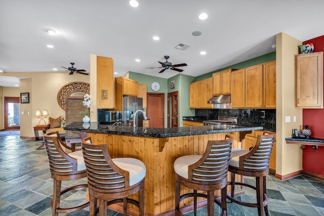 kitchen featuring stone tile floors, under cabinet range hood, ceiling fan, and visible vents