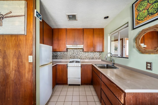 kitchen with white appliances, brown cabinets, a sink, and under cabinet range hood