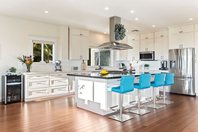 kitchen with beverage cooler, a kitchen island, white cabinetry, stainless steel appliances, and island range hood