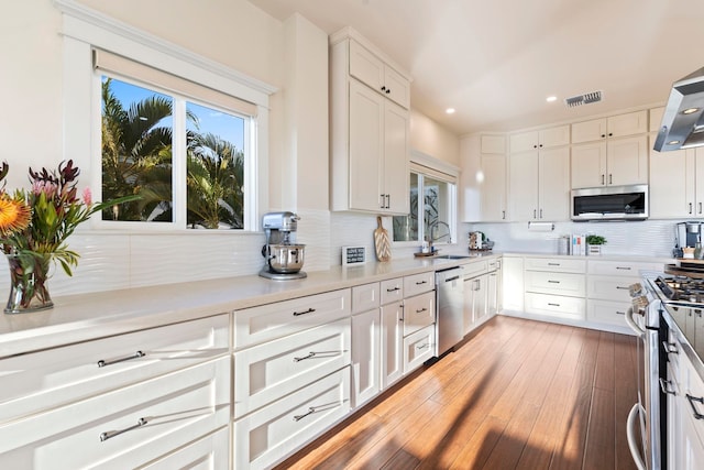 kitchen with light hardwood / wood-style floors, decorative backsplash, sink, white cabinetry, and appliances with stainless steel finishes