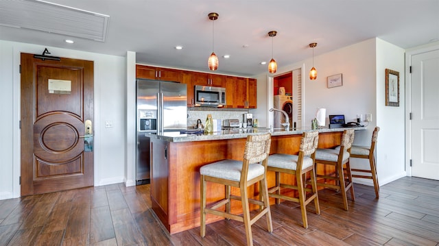 kitchen featuring light stone counters, kitchen peninsula, dark hardwood / wood-style floors, appliances with stainless steel finishes, and decorative light fixtures