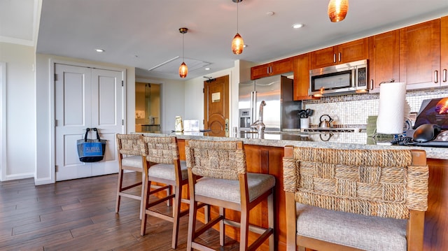 kitchen featuring dark hardwood / wood-style floors, backsplash, a breakfast bar, appliances with stainless steel finishes, and decorative light fixtures