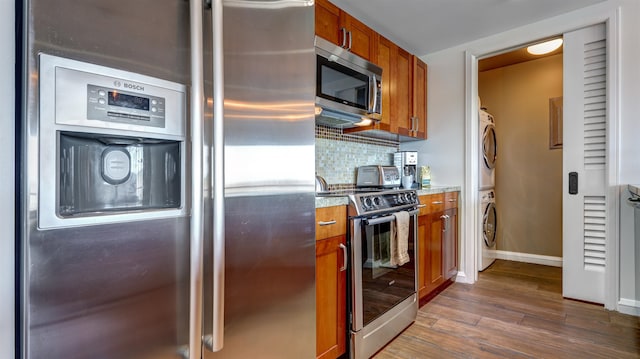 kitchen with dark hardwood / wood-style flooring, stacked washer / drying machine, appliances with stainless steel finishes, and tasteful backsplash