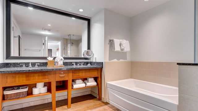 bathroom featuring vanity, hardwood / wood-style flooring, and a tub to relax in