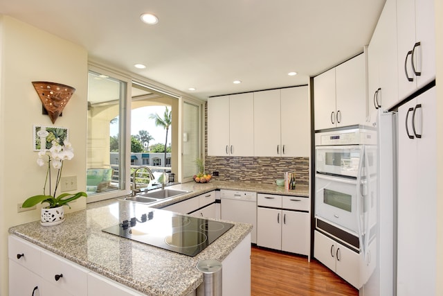 kitchen with kitchen peninsula, white appliances, white cabinetry, and sink