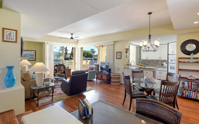 living room with ceiling fan with notable chandelier, light hardwood / wood-style floors, and sink