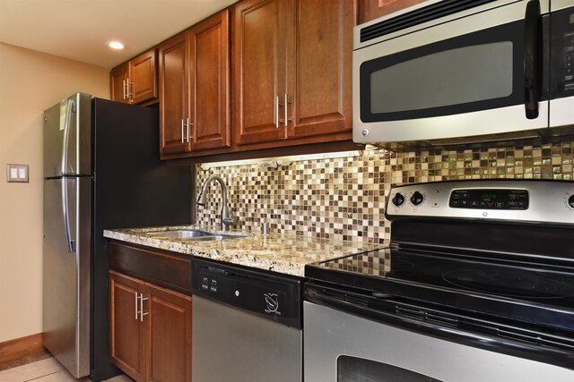 kitchen featuring stainless steel appliances, backsplash, light tile floors, sink, and light stone countertops