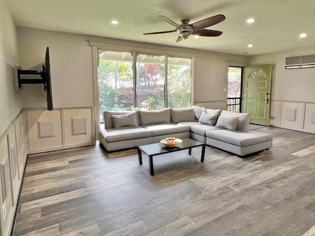 living area with a decorative wall, wood finished floors, a wainscoted wall, and ceiling fan