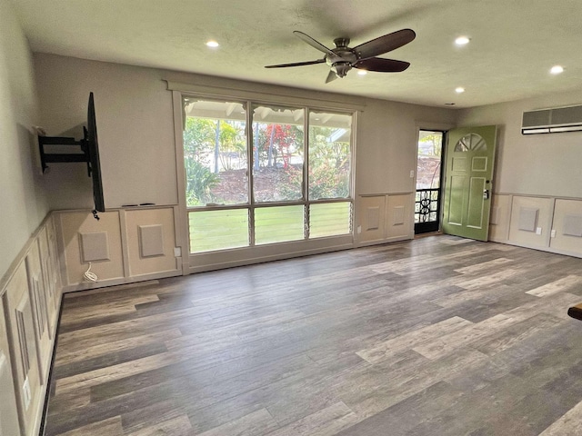 unfurnished living room featuring a ceiling fan, a decorative wall, wood finished floors, and a wall mounted AC