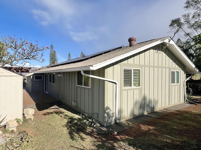 view of side of property featuring solar panels, board and batten siding, and a shingled roof