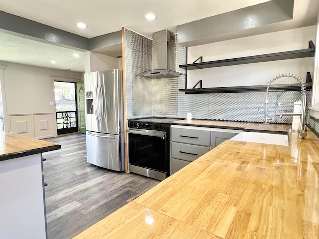 kitchen featuring butcher block countertops, range with electric stovetop, wood finished floors, stainless steel fridge, and wall chimney range hood