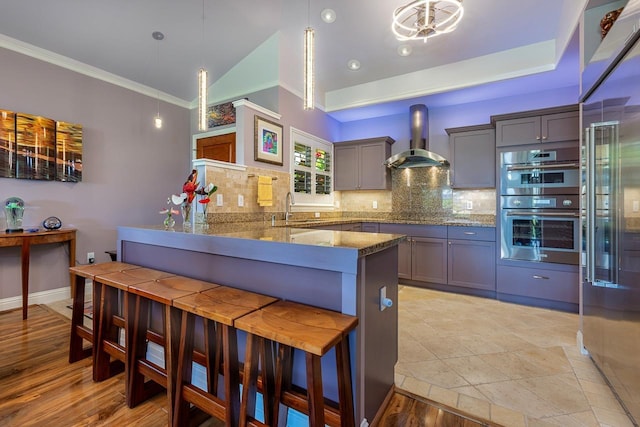 kitchen with kitchen peninsula, decorative light fixtures, sink, wall chimney range hood, and a kitchen breakfast bar