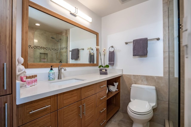 bathroom featuring vanity, tile patterned flooring, toilet, tiled shower, and tile walls