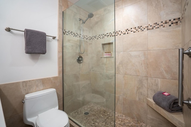 bathroom with tiled shower, toilet, and tile walls