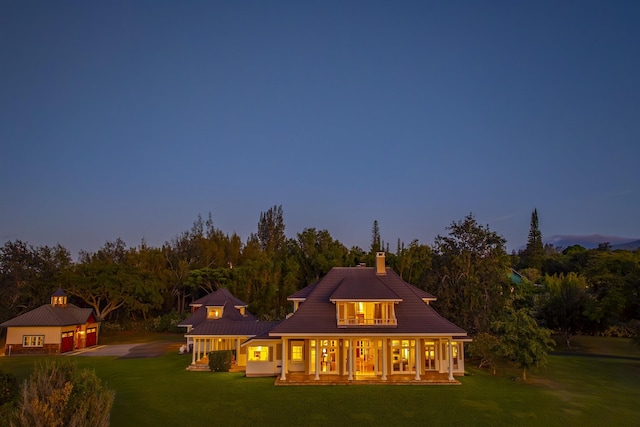 back house at dusk with covered porch and a lawn