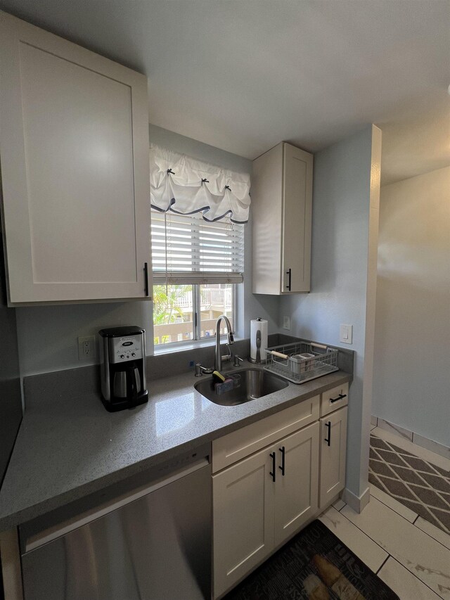 kitchen with sink, white cabinets, stainless steel dishwasher, and dark tile patterned flooring