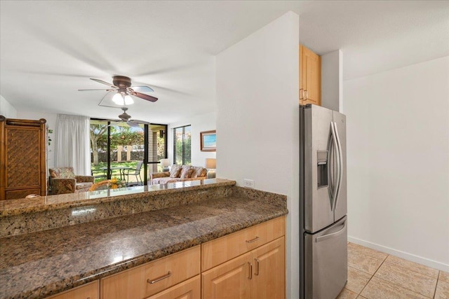 kitchen featuring dark stone countertops, light tile patterned flooring, ceiling fan, light brown cabinetry, and stainless steel fridge