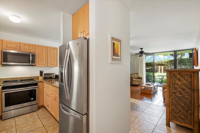 kitchen featuring stone counters, a ceiling fan, light brown cabinets, open floor plan, and appliances with stainless steel finishes