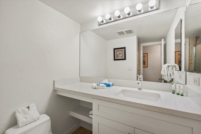 bathroom featuring toilet, vanity, a textured ceiling, visible vents, and a textured wall