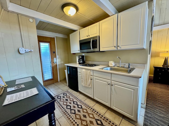 kitchen with wood walls, light tile patterned floors, white cabinetry, beamed ceiling, and sink