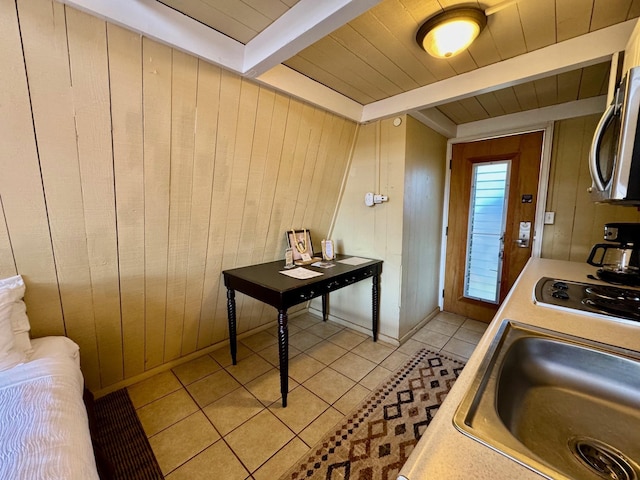 kitchen featuring stovetop, wood walls, light tile patterned flooring, beamed ceiling, and sink