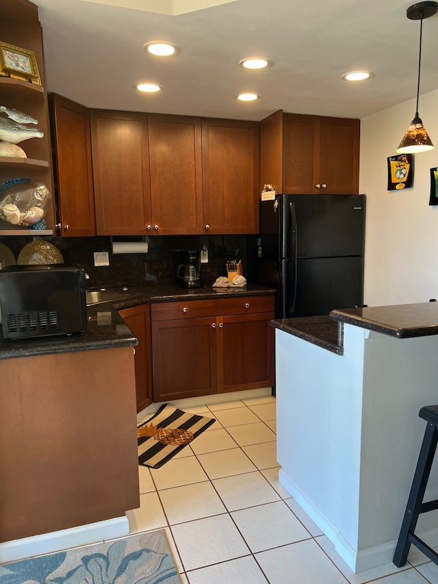 kitchen featuring dark stone counters, decorative light fixtures, decorative backsplash, black refrigerator, and light tile patterned floors